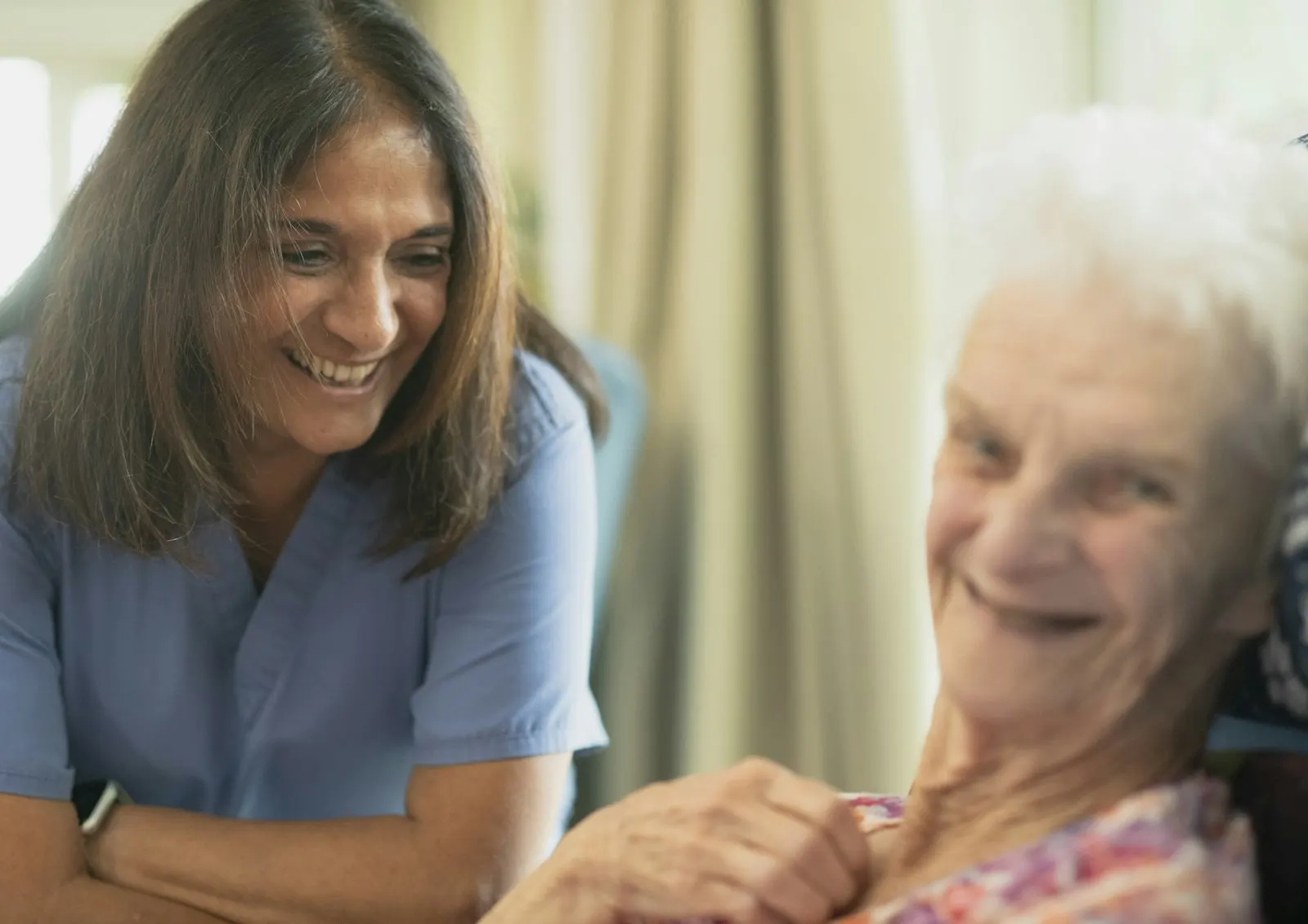 A smiling carer sitting with an older woman