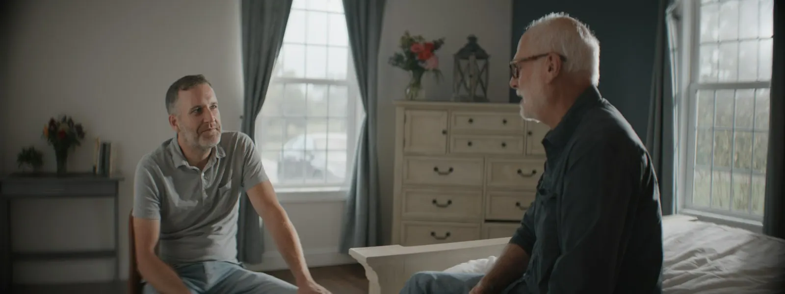 A man talking with his elderly father in a sunlit bedroom