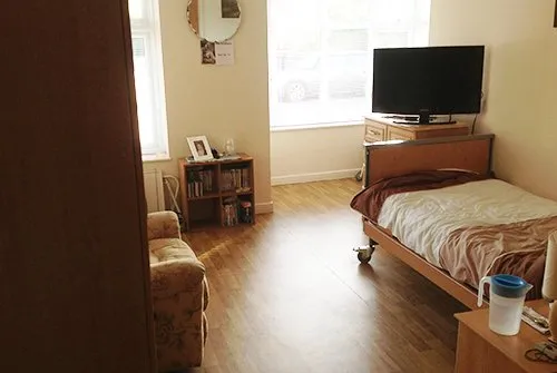 A bedroom with a television, armchair and bookshelf, photographed when the home opened