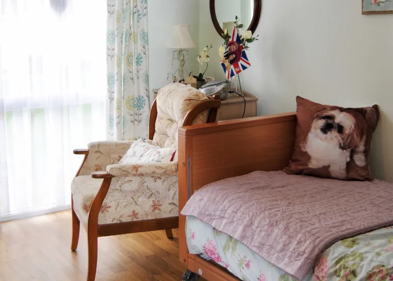 A resident's bedroom with an armchair, a dog-print cushion and a dressing table by the window