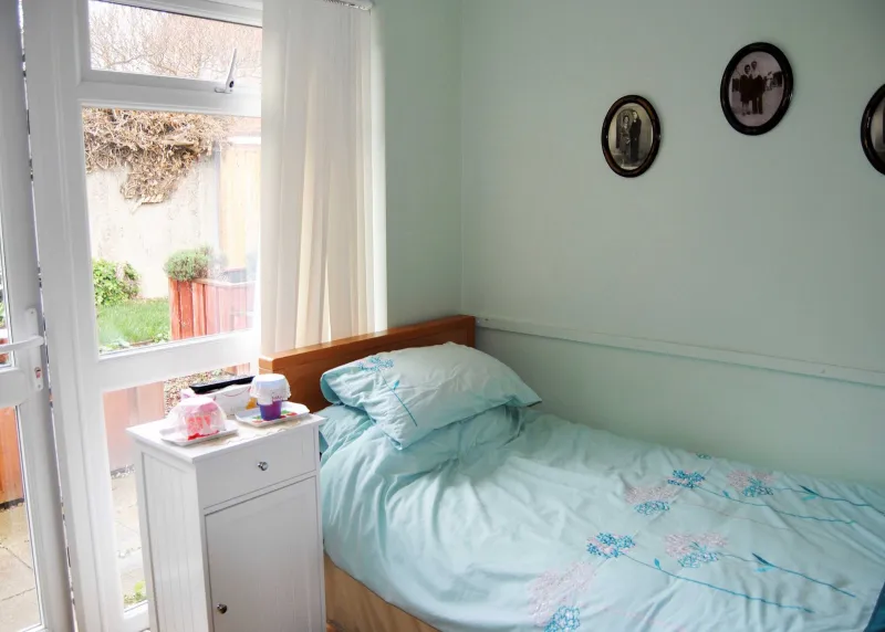 A single bedroom with a patio door to the garden, a bedside cabinet and family portraits on the wall