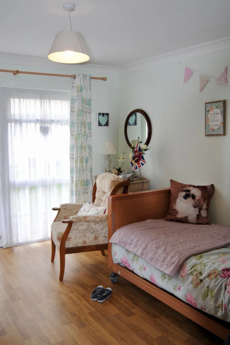 A bedroom with patio doors, an armchair, a mirror and bunting along the wall