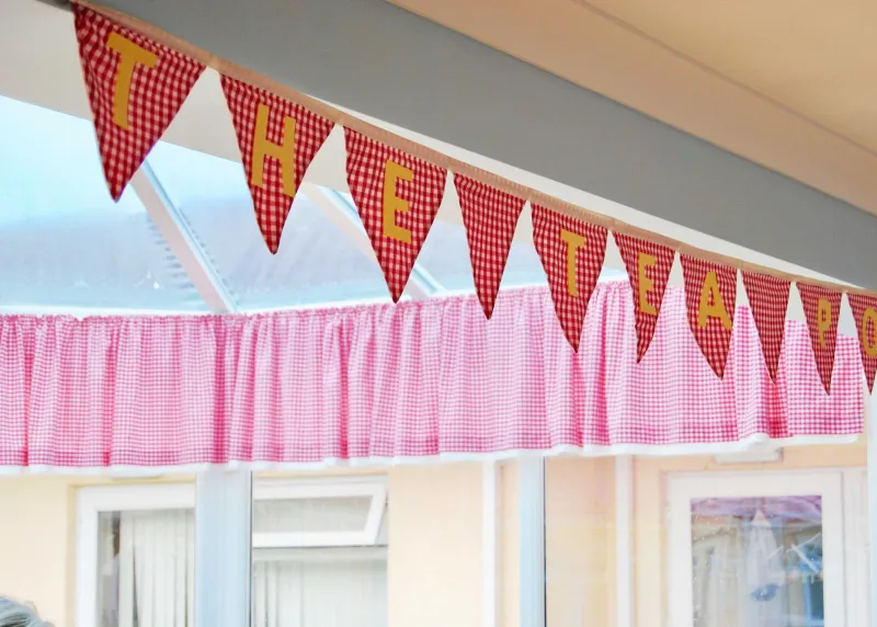 Red and white gingham bunting spelling out a sign in the conservatory tea area