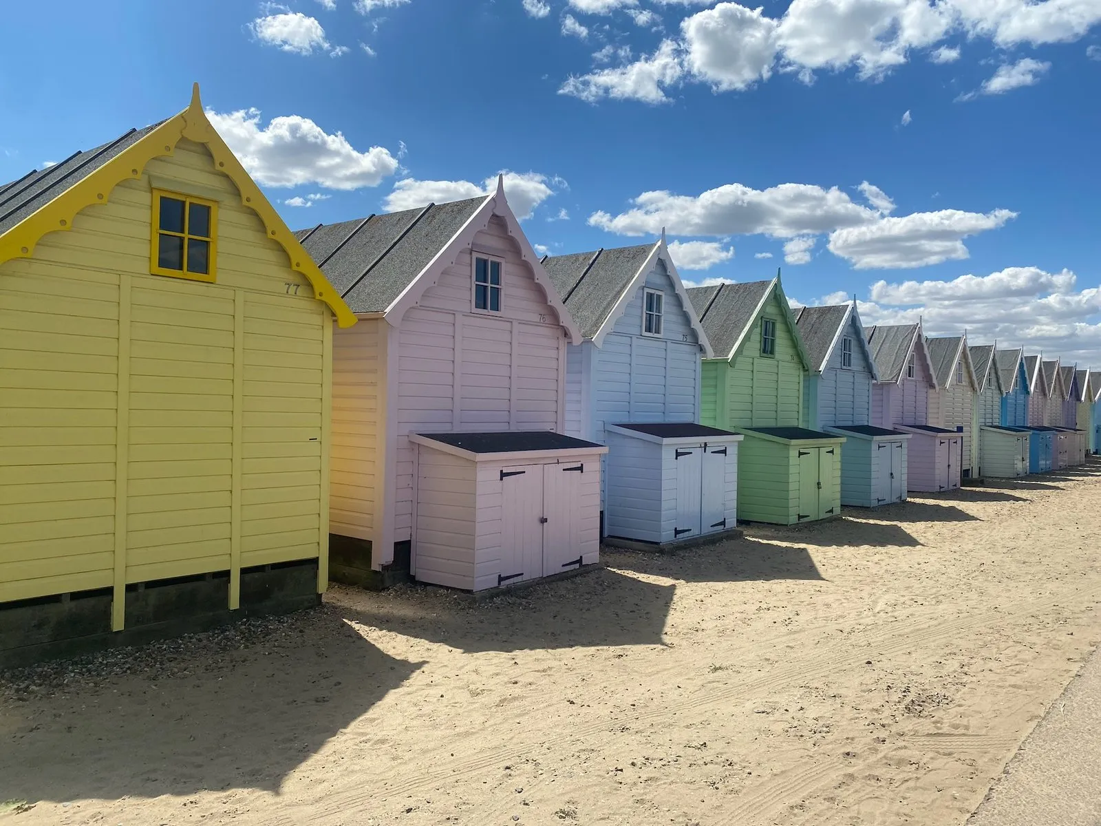 A row of pastel beach huts on the sand under a blue sky
