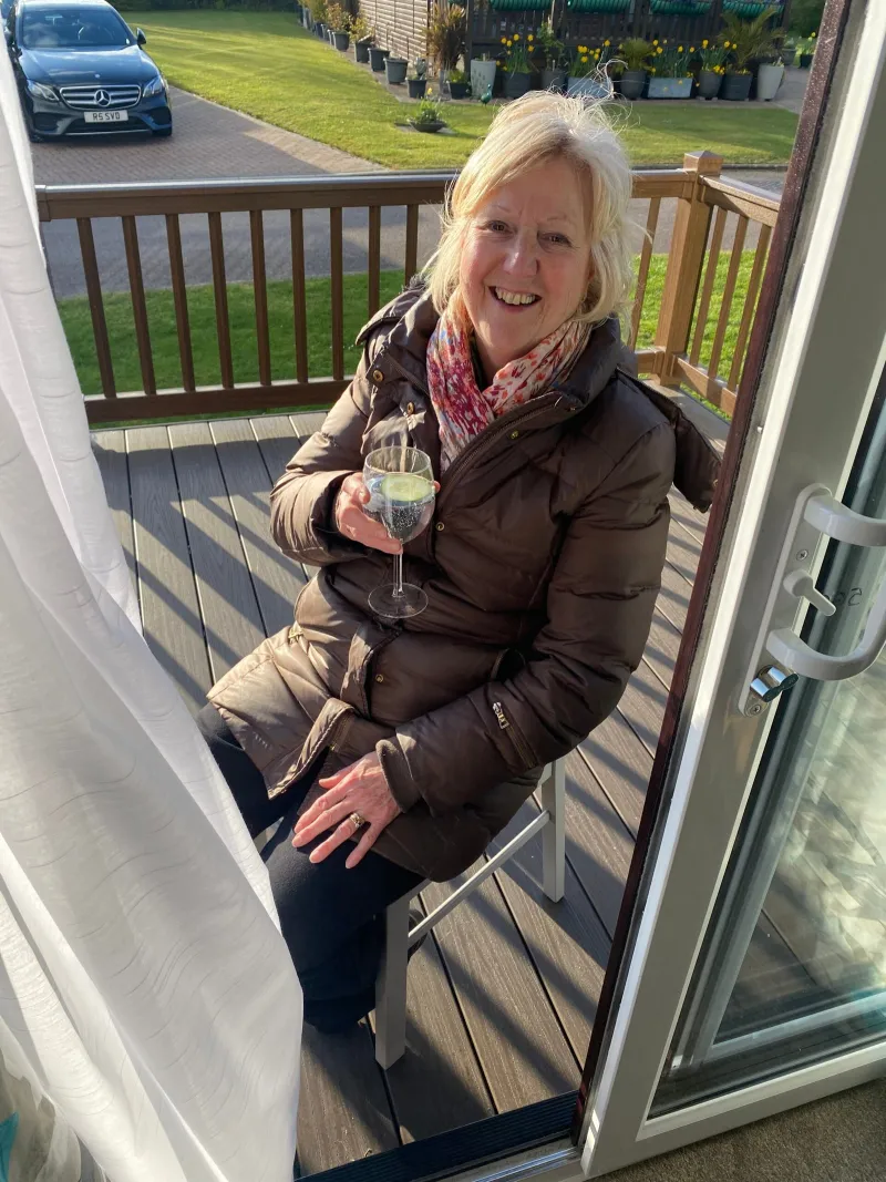 A woman relaxing with a drink on the decking of a holiday caravan