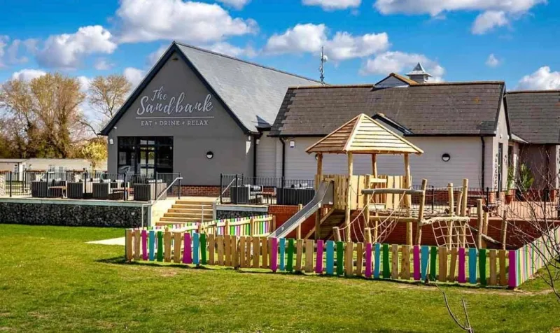 The Sandbank clubhouse with a wooden play area and a rainbow-painted fence
