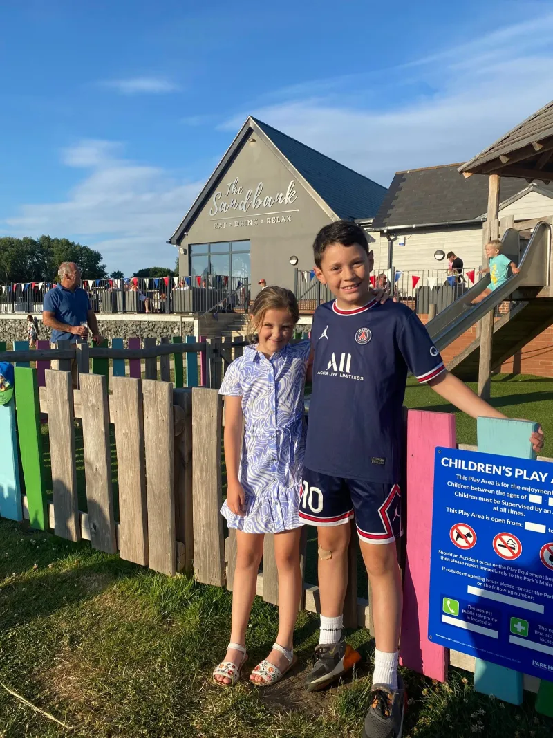 Two children standing by the fence of a children's play area at a holiday park