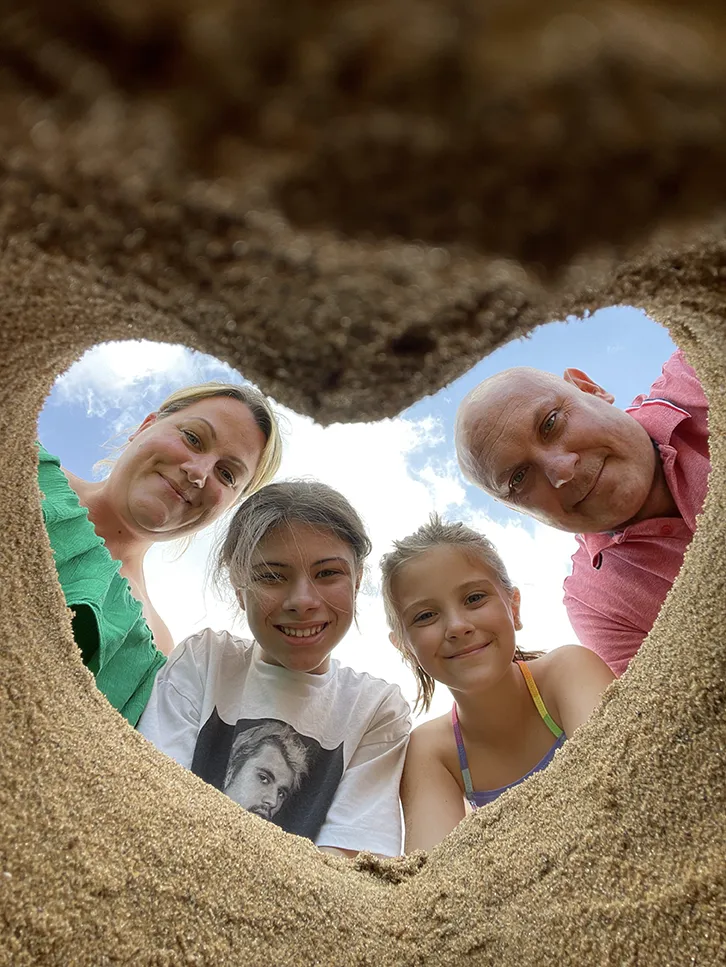 A family looking down into a heart-shaped hole in the sand