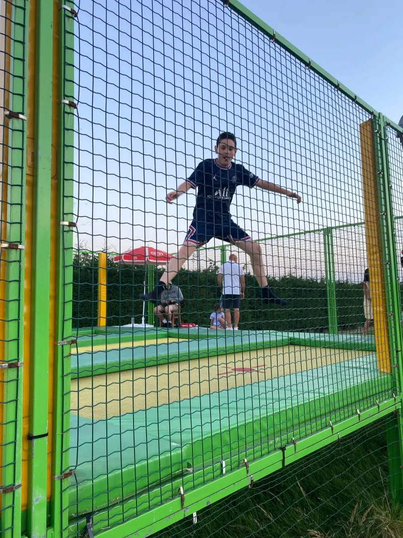A boy jumping on a trampoline inside a netted enclosure