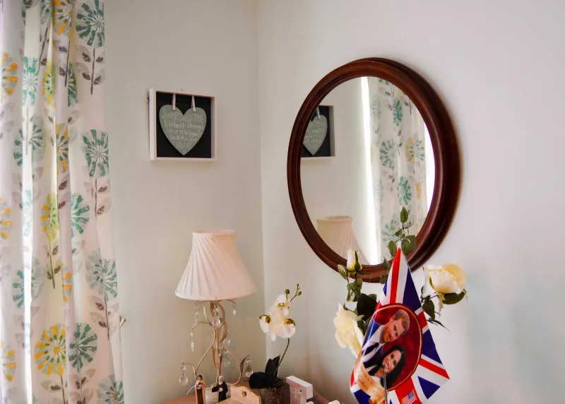 A dressing table with a lamp, flowers, a round mirror and a royal wedding keepsake
