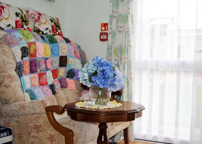 An armchair with a hand-made patchwork blanket beside a table with blue hydrangeas