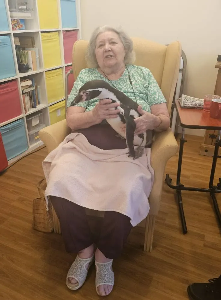 A resident holding a penguin on her lap in front of a colourful bookcase