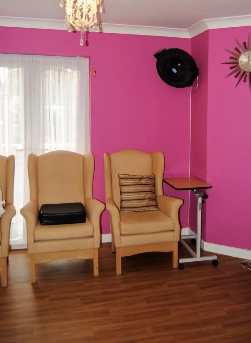 Wing-back armchairs against a pink wall below a sunburst clock