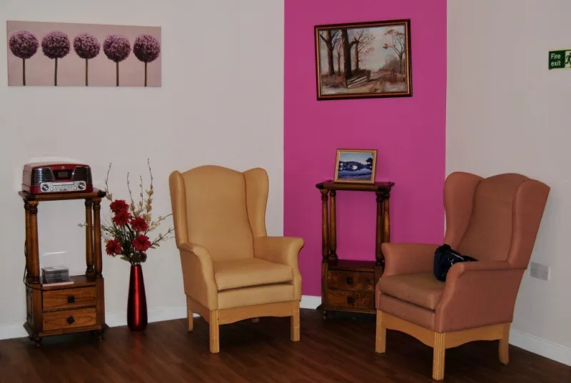 A seating corner with two wing-back armchairs, a radio and a painting on a pink feature wall