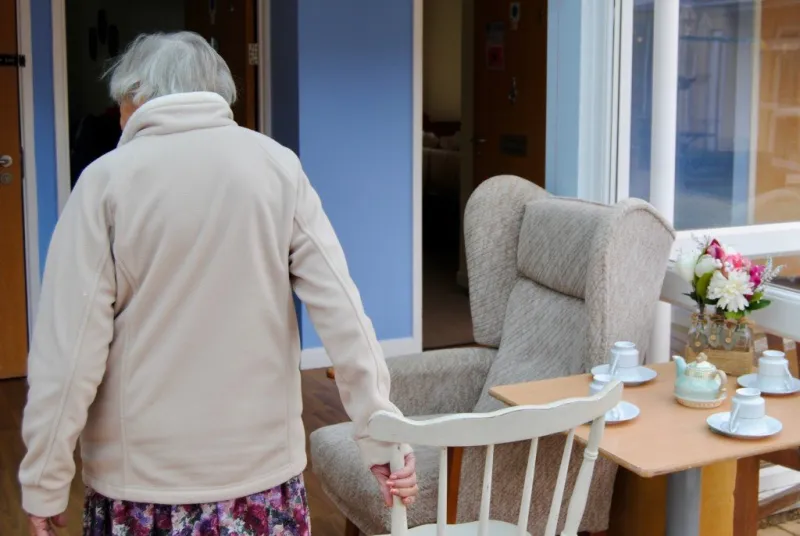 A resident walking to a table set for tea in the conservatory