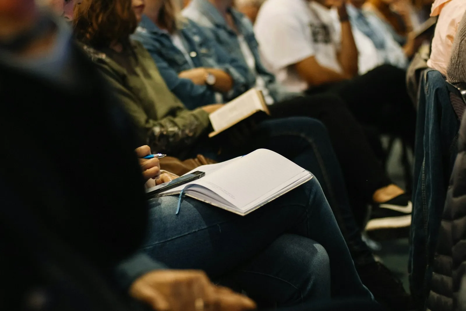 People seated in rows at a seminar, taking notes in notebooks