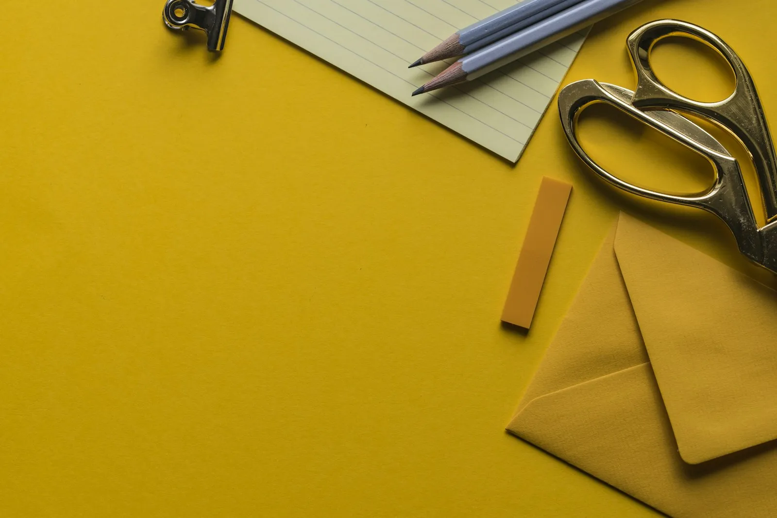 Notepaper, pencils, scissors and an envelope on a yellow desk